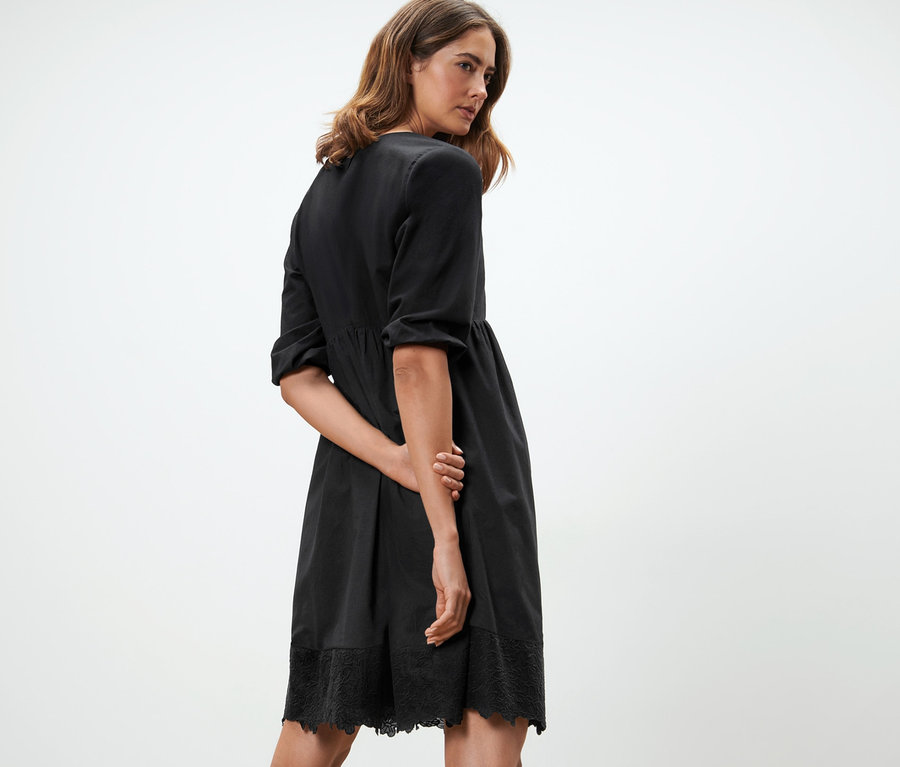 Nő pózol fekete, hímzett szövött ruhában.