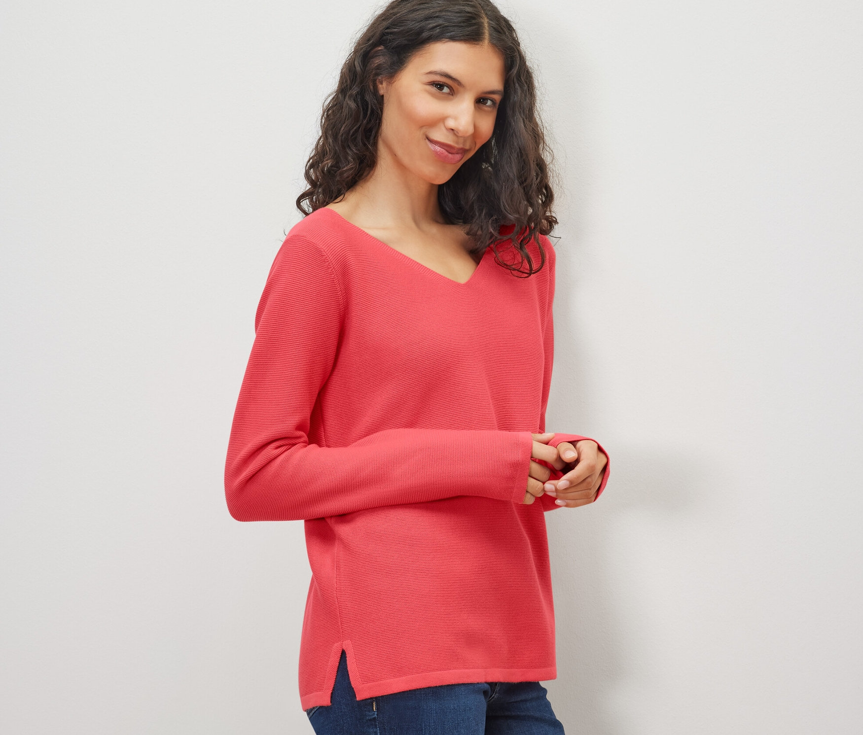 Nő korall kötött pulóvert és farmert visel.