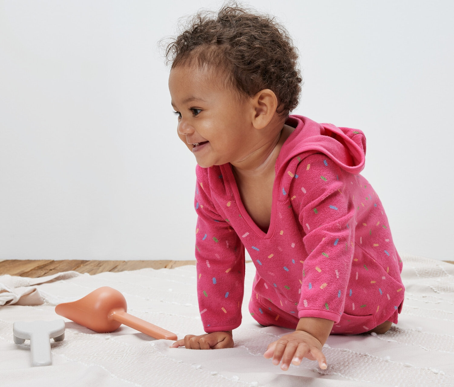 Kisgyermek mászik egy takarón, rózsaszín frottír poncsót visel.