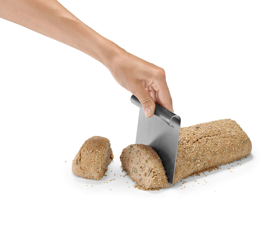 Egy kéz egy magvakkal megszórt kenyérkenyeret vág egy fémkéssel.