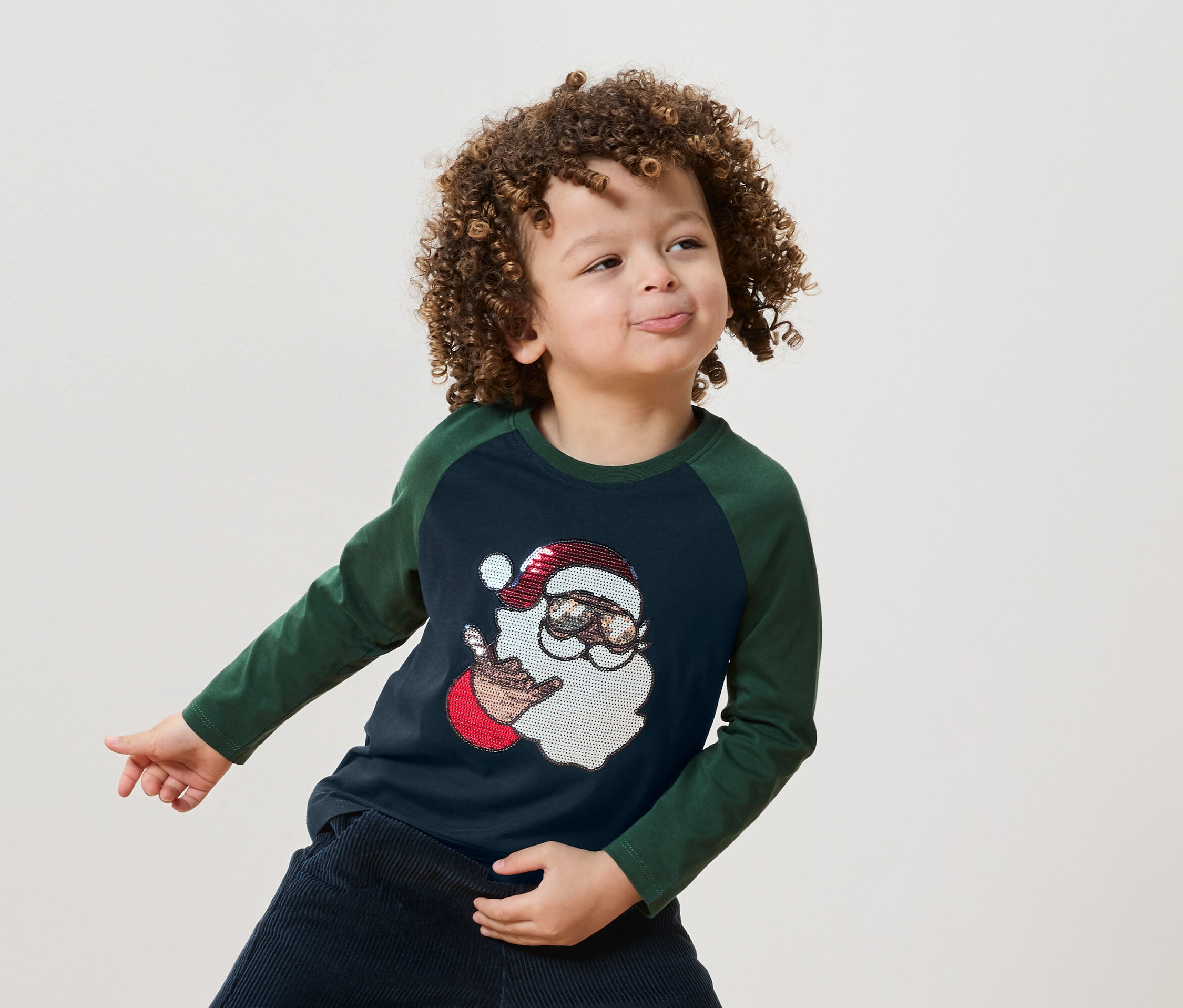 Egy göndör hajú fiú kék-zöld pólót visel, melyen a Mikulás képe látható.