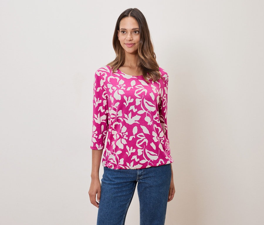 Nő virágmintás rózsaszín felsőt és farmert visel.