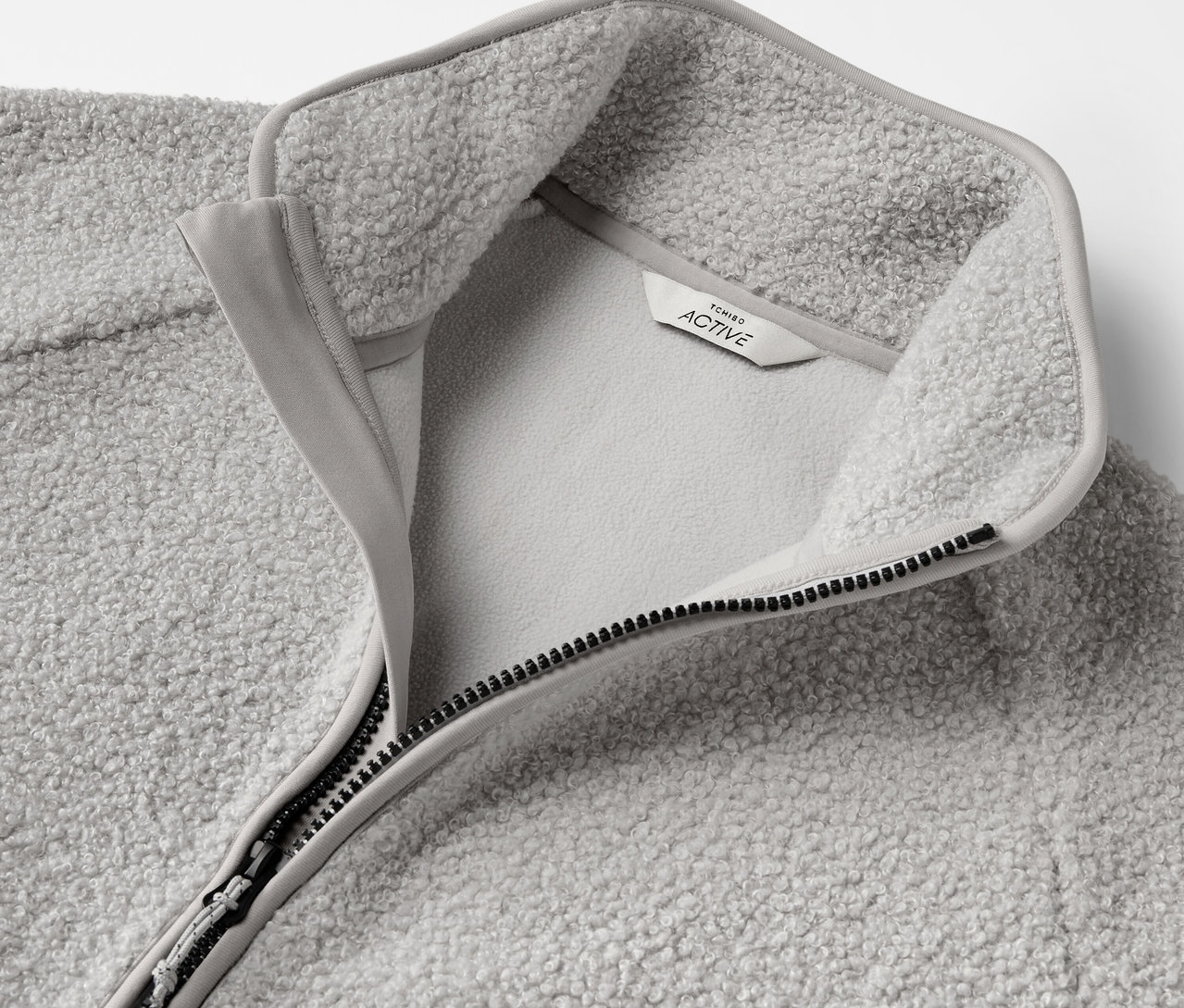 Egy szürke, cipzáros fleece pulóver részletgazdag képe, rajta egy címkével.