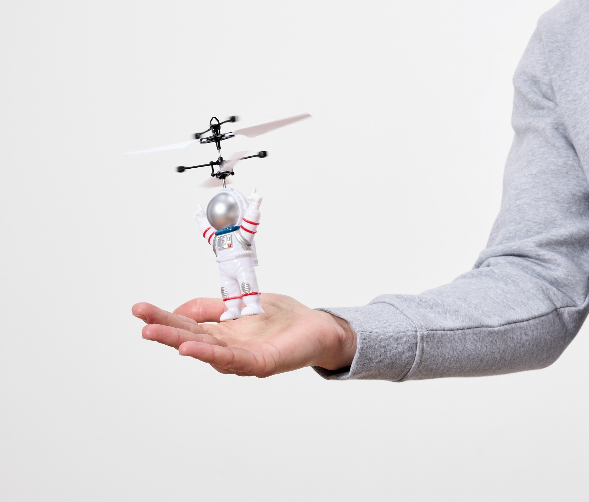 Egy tenyéren egy kis űrhajós játék helikopterrel a feje fölött.