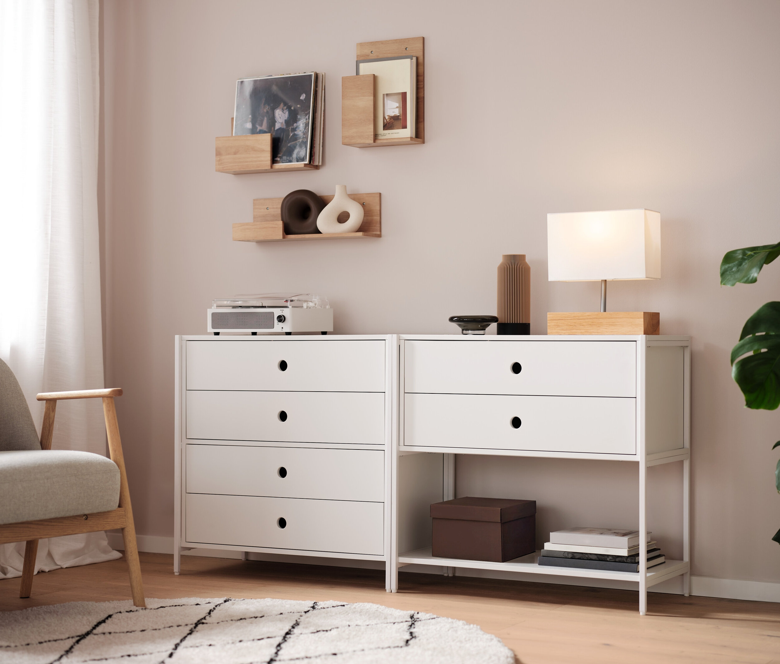 Két fehér komód áll egymás mellett, rajtuk egy lámpa, egy váza és egy rádió. A falon polcok vannak.