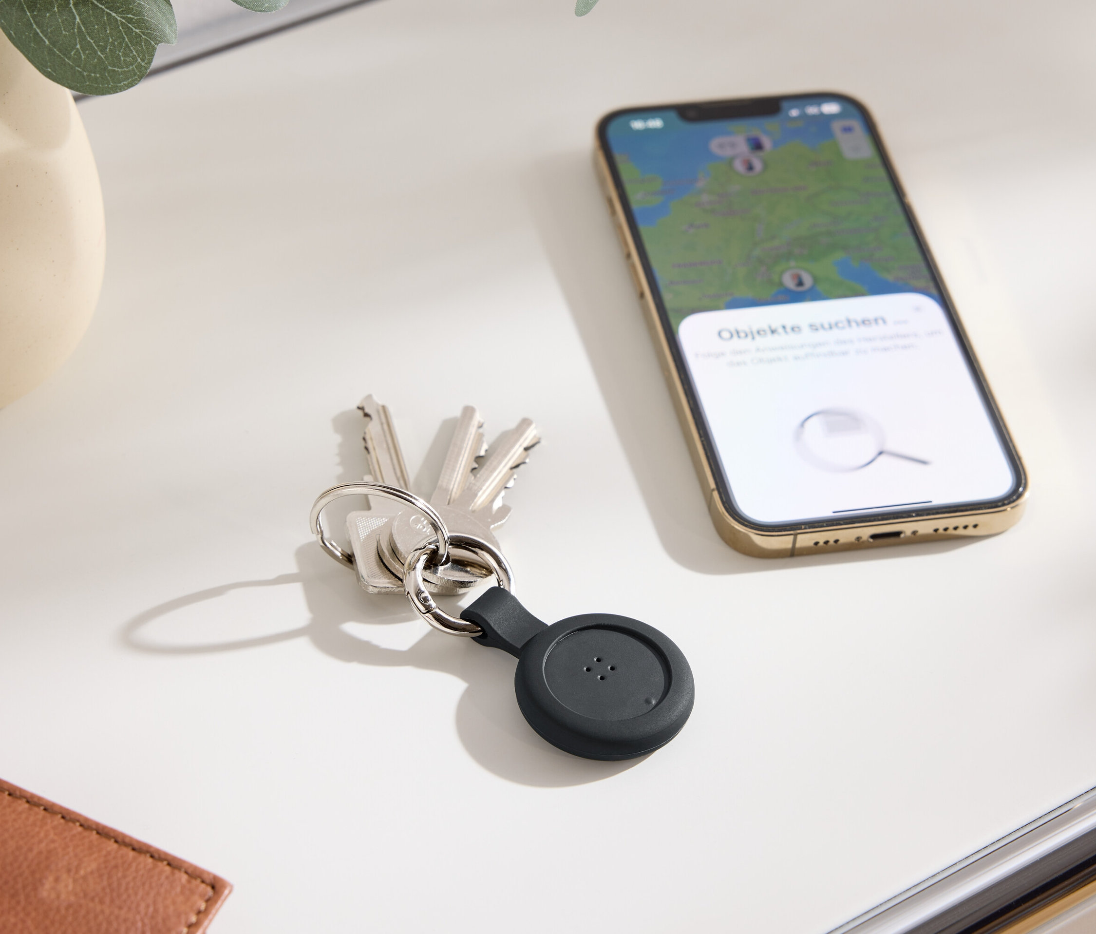 Kulcsok fekete nyomkövetővel és egy mobiltelefon térképpel a kijelzőn egy asztalon.