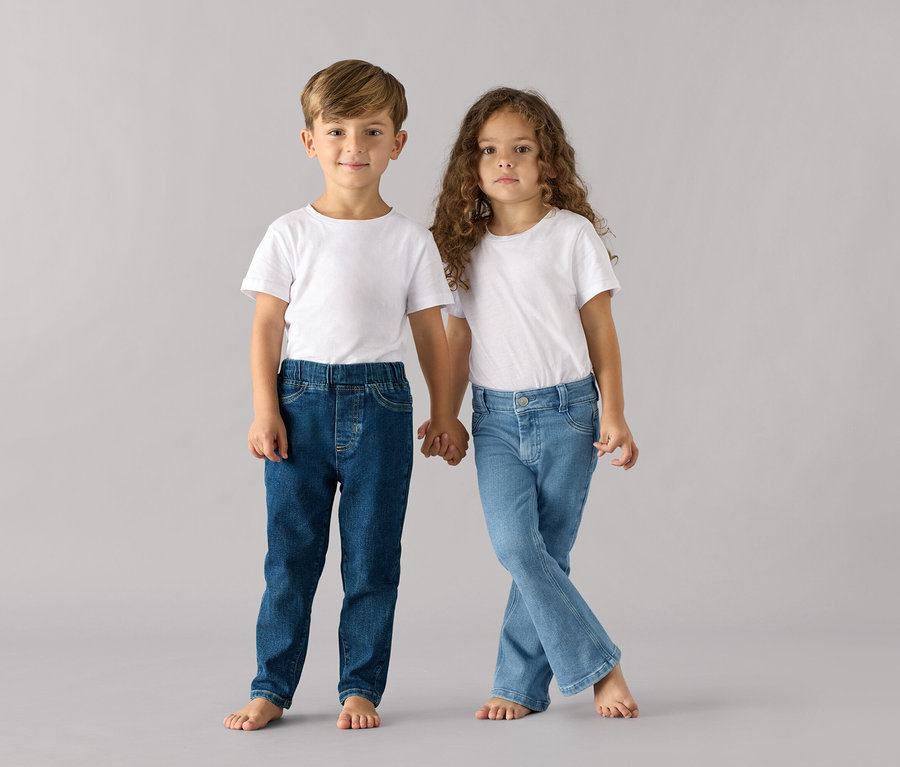 Egy fiú és egy lány kézenfogva állnak, mindketten fehér pólót és Belebújós nadrág gyerekeknek – Fit »Luca« nadrágot viselnek.