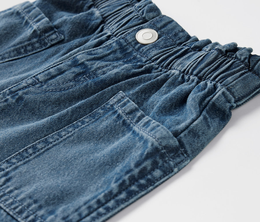 Egy farmer rövidnadrág részlete, elasztikus derékpánttal és zsebekkel.