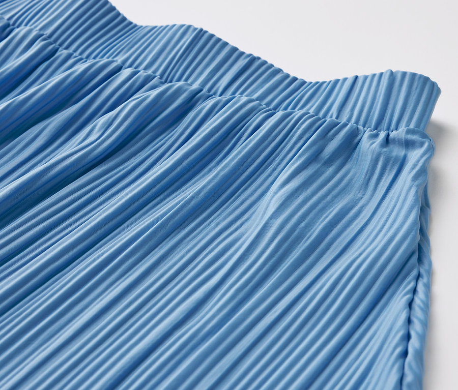 Egy kék pliszírozott szoknya részlete.