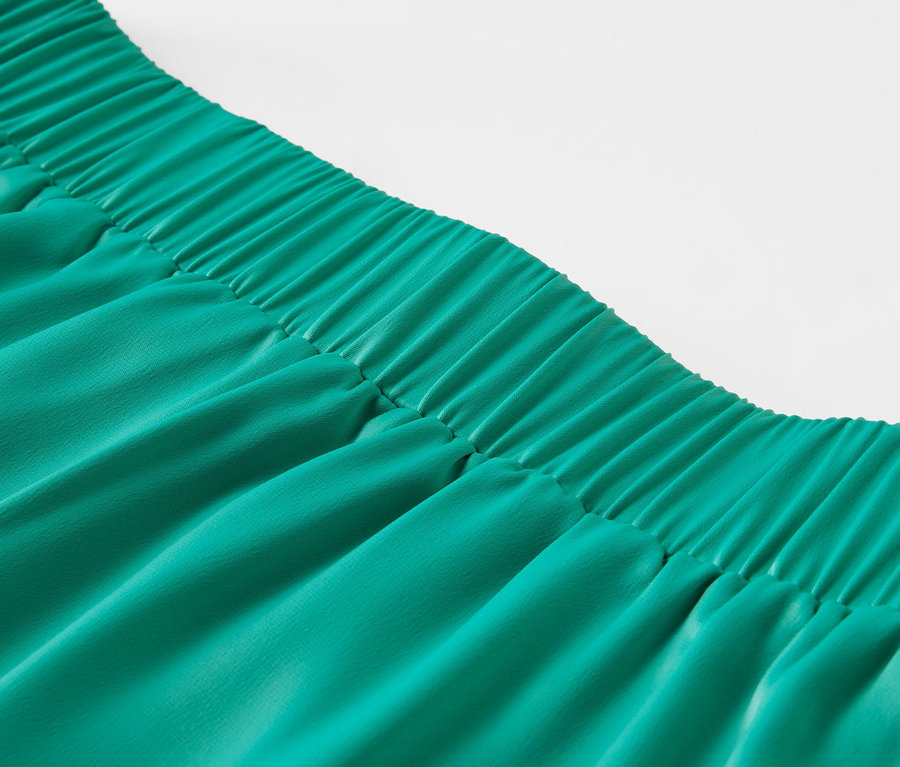 Egy zöld, gumis derekú szaténszoknya közeli képe.