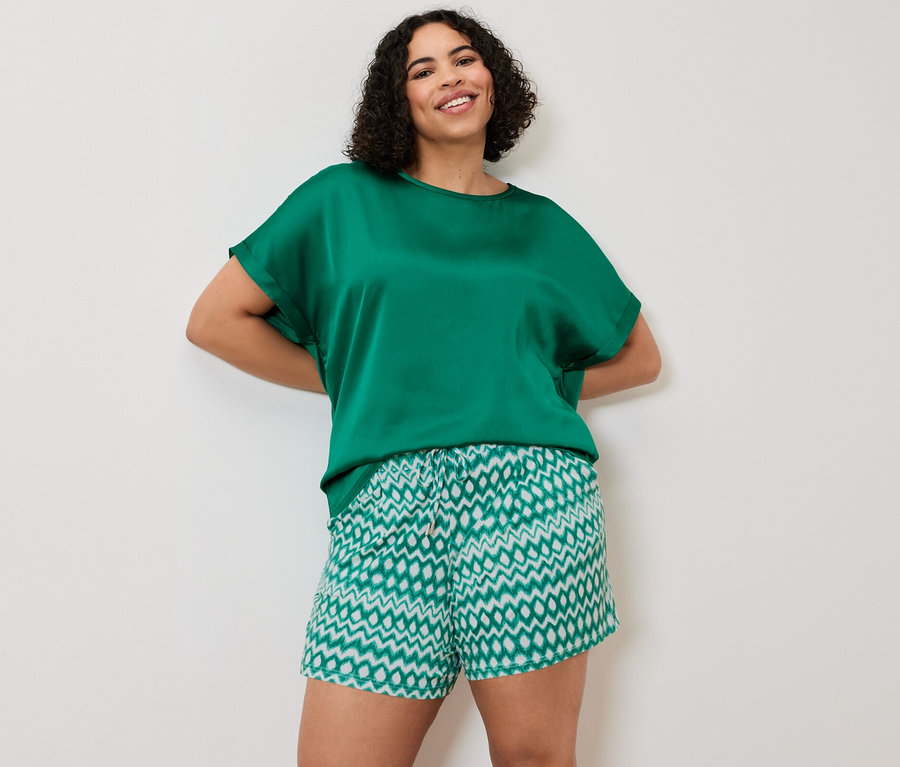 Nő pózol egy vízkék, többféle anyagból készült ingblúzban és 2 jersey rövidnadrágban.