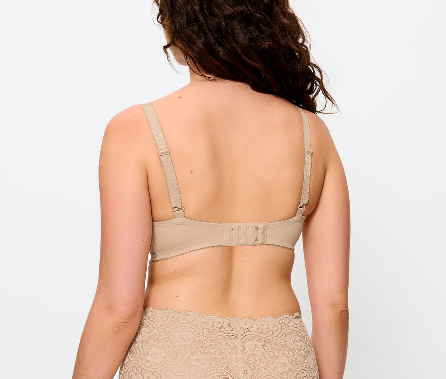 Hátulnézet egy barna, hullámos hajú nőről, aki bézs melltartót és csipkés bugyit visel.