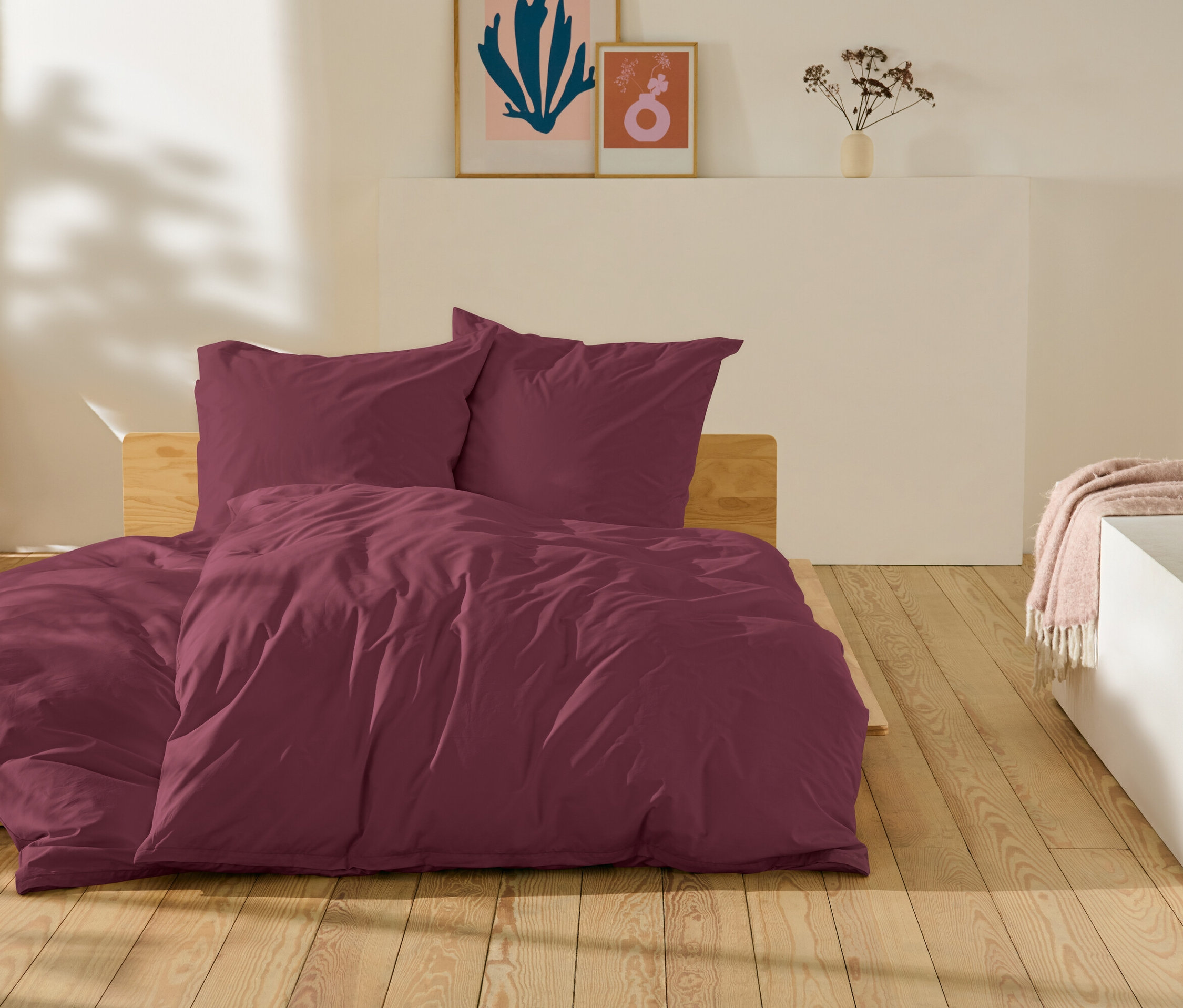 Bordó ágynemű fekszik egy ágyon egy fa padlón.
