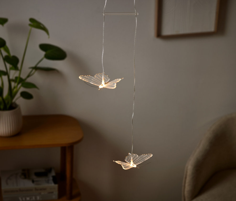 Két pillangó alakú lámpa lóg egy szobában, mellette egy cserepes növény.