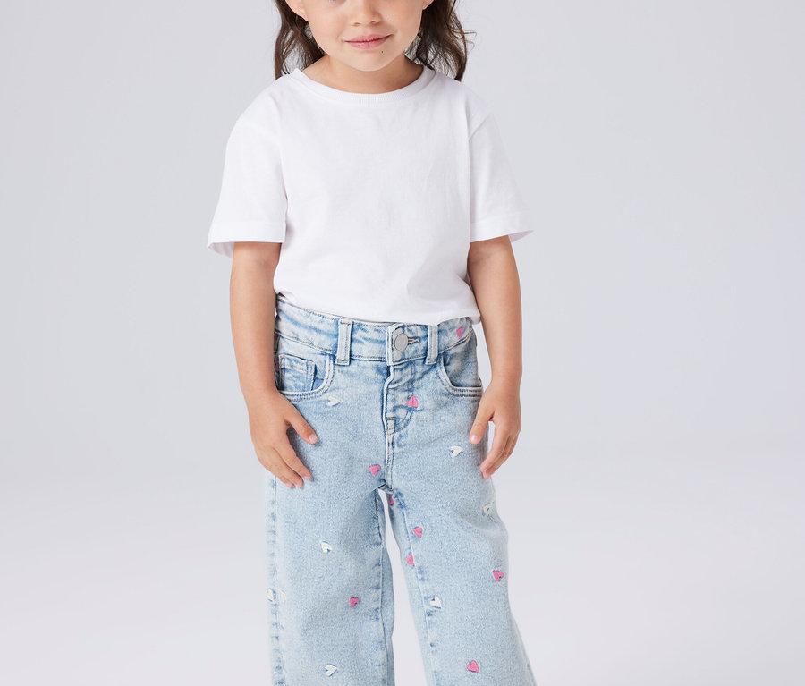 Kislány fehér pólóban és világoskék, szívecskés és egérmintás farmerben.