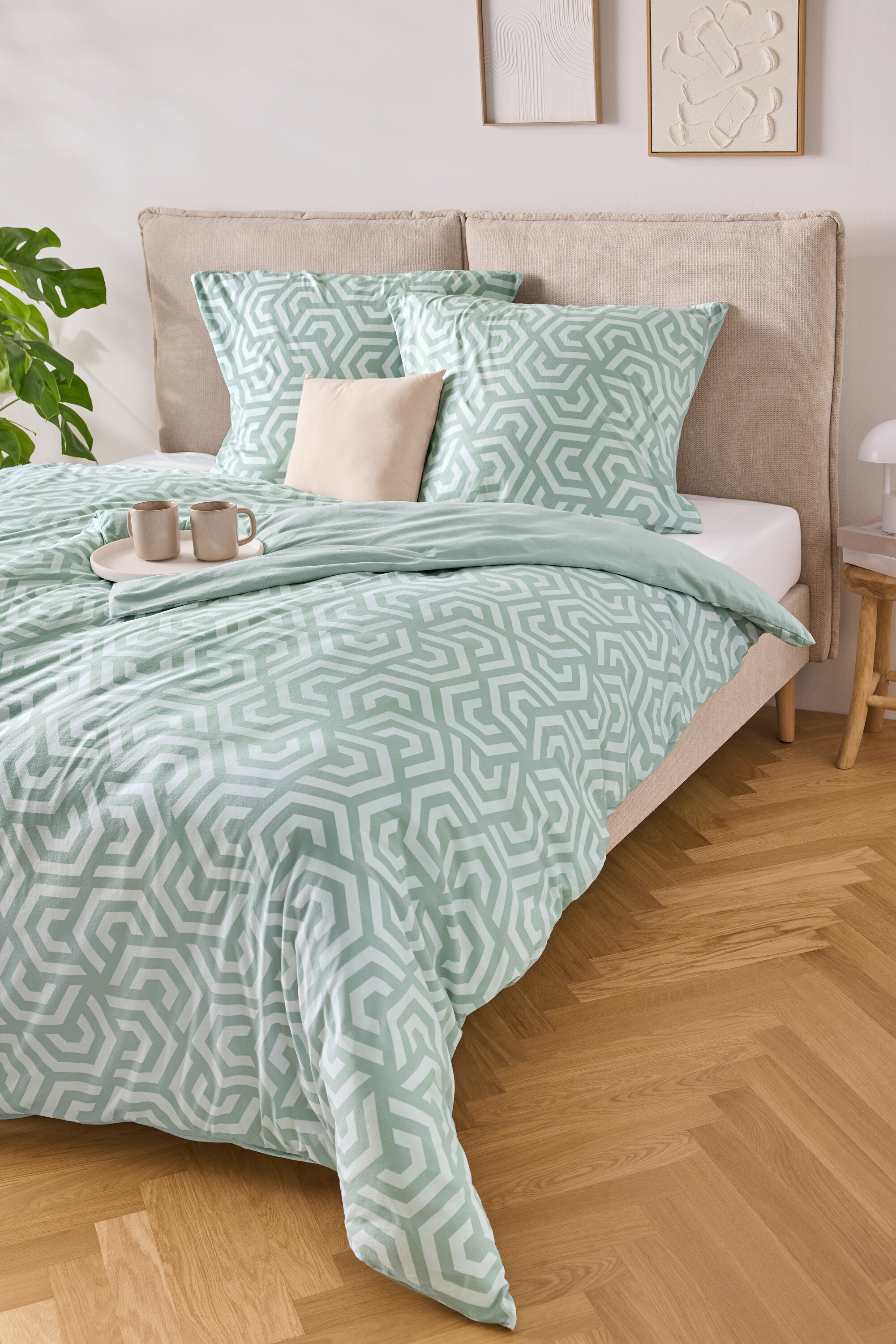 Egy ágy világoskék-fehér csíkos ágyneművel, két párnával és egy tálcával, rajta két csészével.