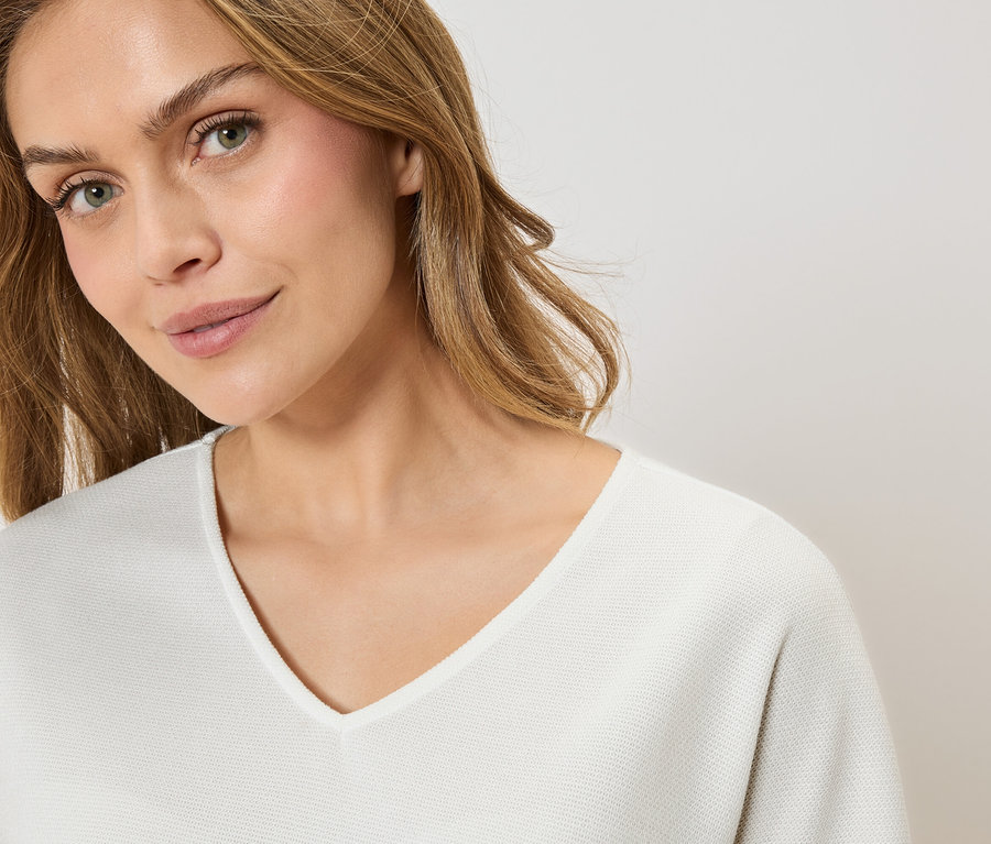 Portré egy szőke hajú nő fehér, V-nyakú pulóverben.
