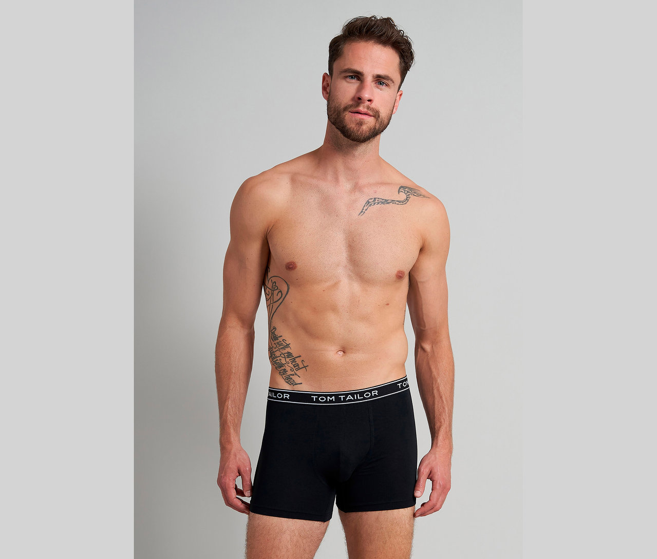Felsőtestén tetovált férfi fekete TOM TAILOR boxeralsóban.
