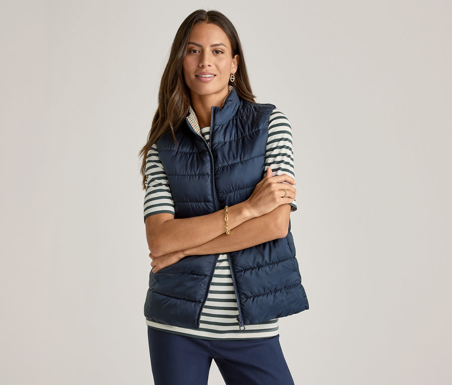 A karjait keresztbe tevő nő tengerészkék mellényt visel egy zöld csíkos, félhosszú ujjú felső fölött.