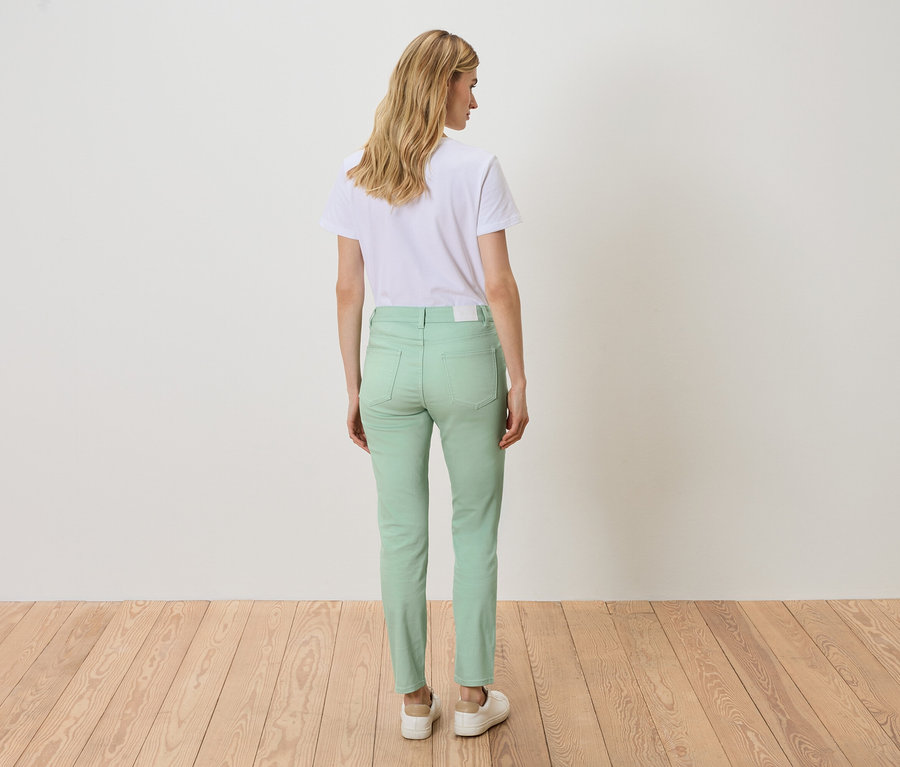 Hátulnézet egy szőke hajú nőről, aki fehér pólót és világoszöld farmert visel.