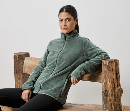 Nő ül egy fa padon, zöld polár pulóvert és fekete leggingset visel.