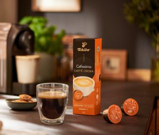 Kávéfőző egy pohár kávé és egy csomag Caffè Crema Rich aroma – 10 db kávékapszula mellett.
