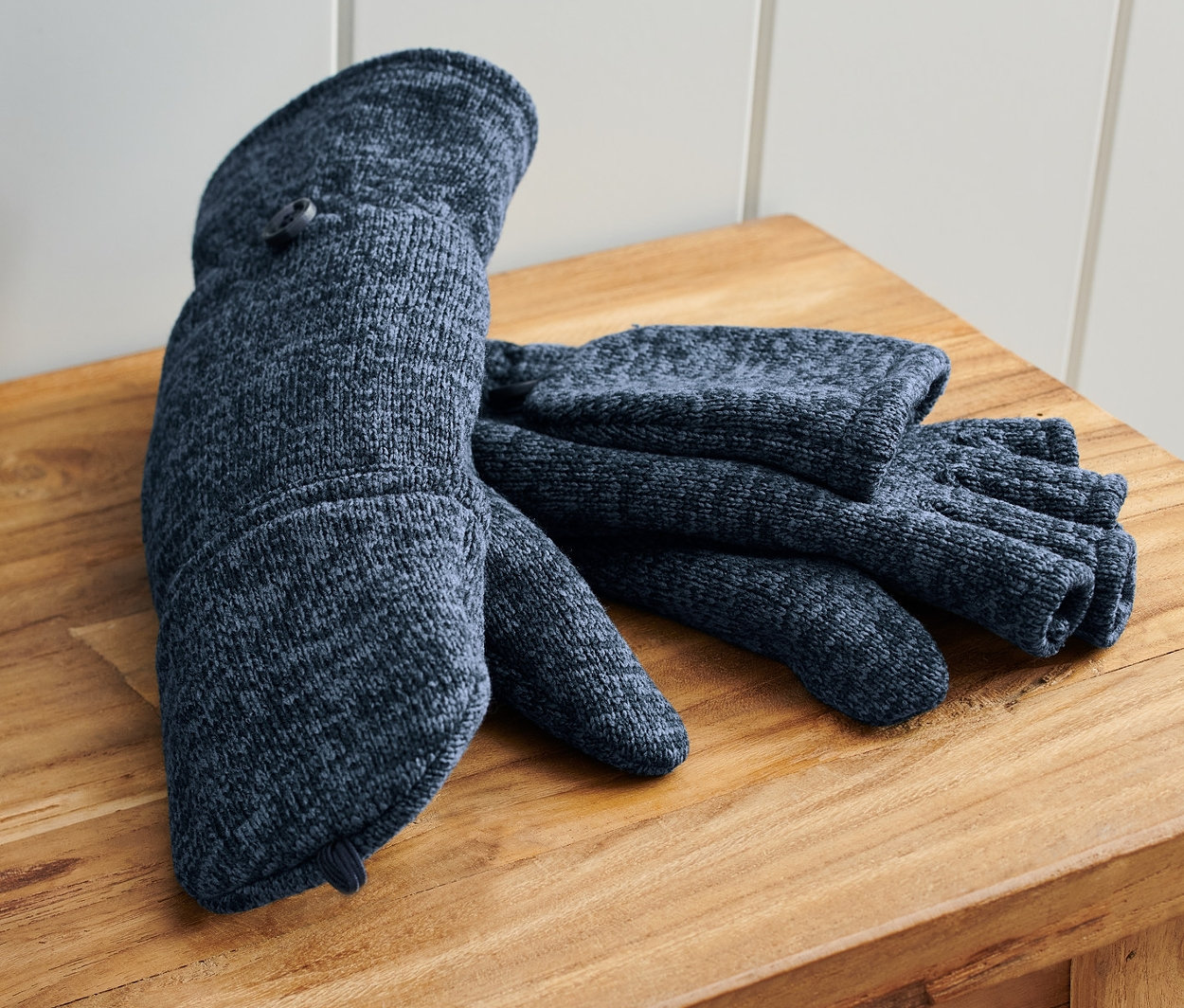 Egy pár kék, lehajtható egyujjas kesztyű egy fa padon fekszik egy kék táska mellett.