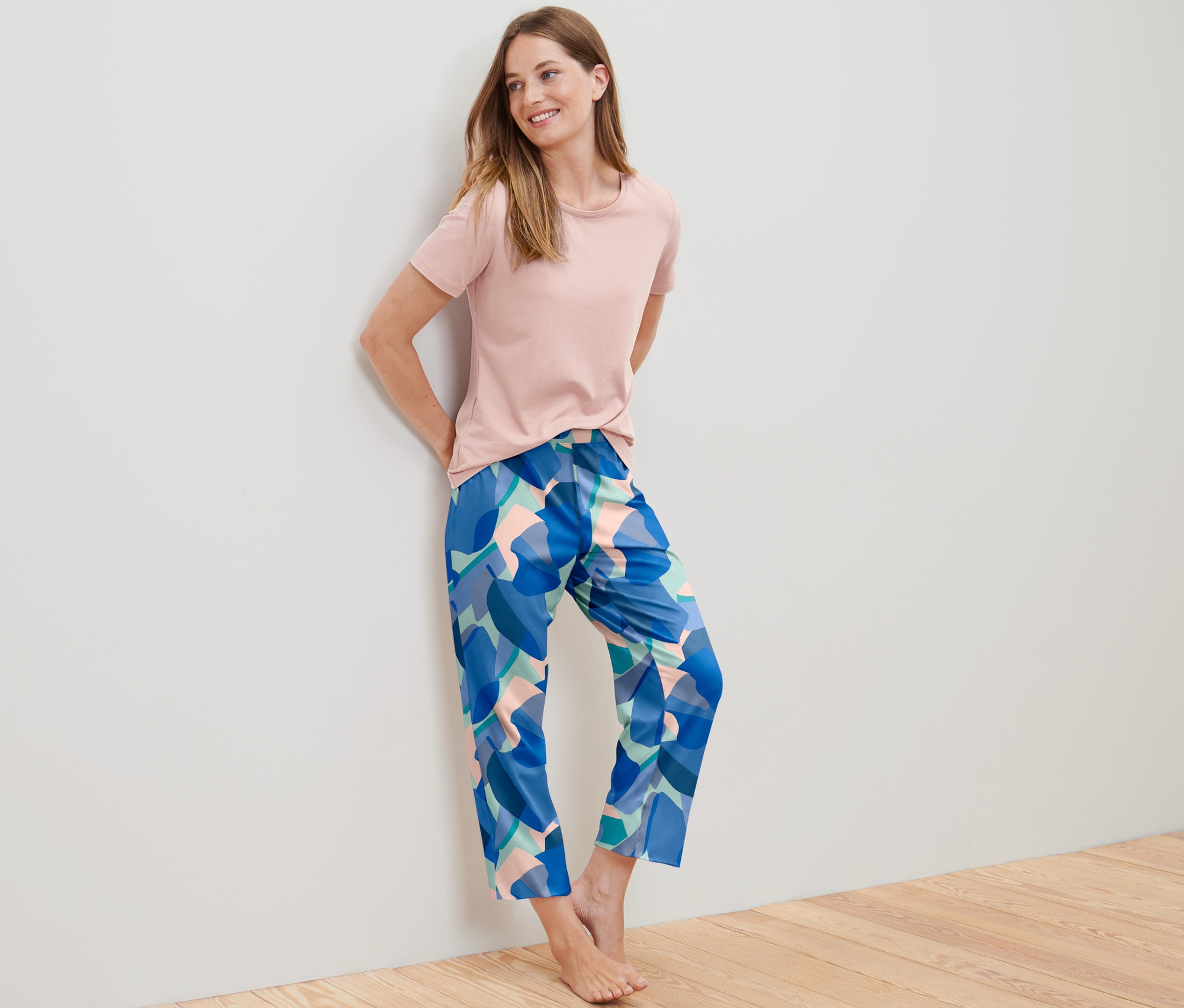 Falnak támaszkodó nő mintás, rózsaszín női 7/8-os pizsamában.