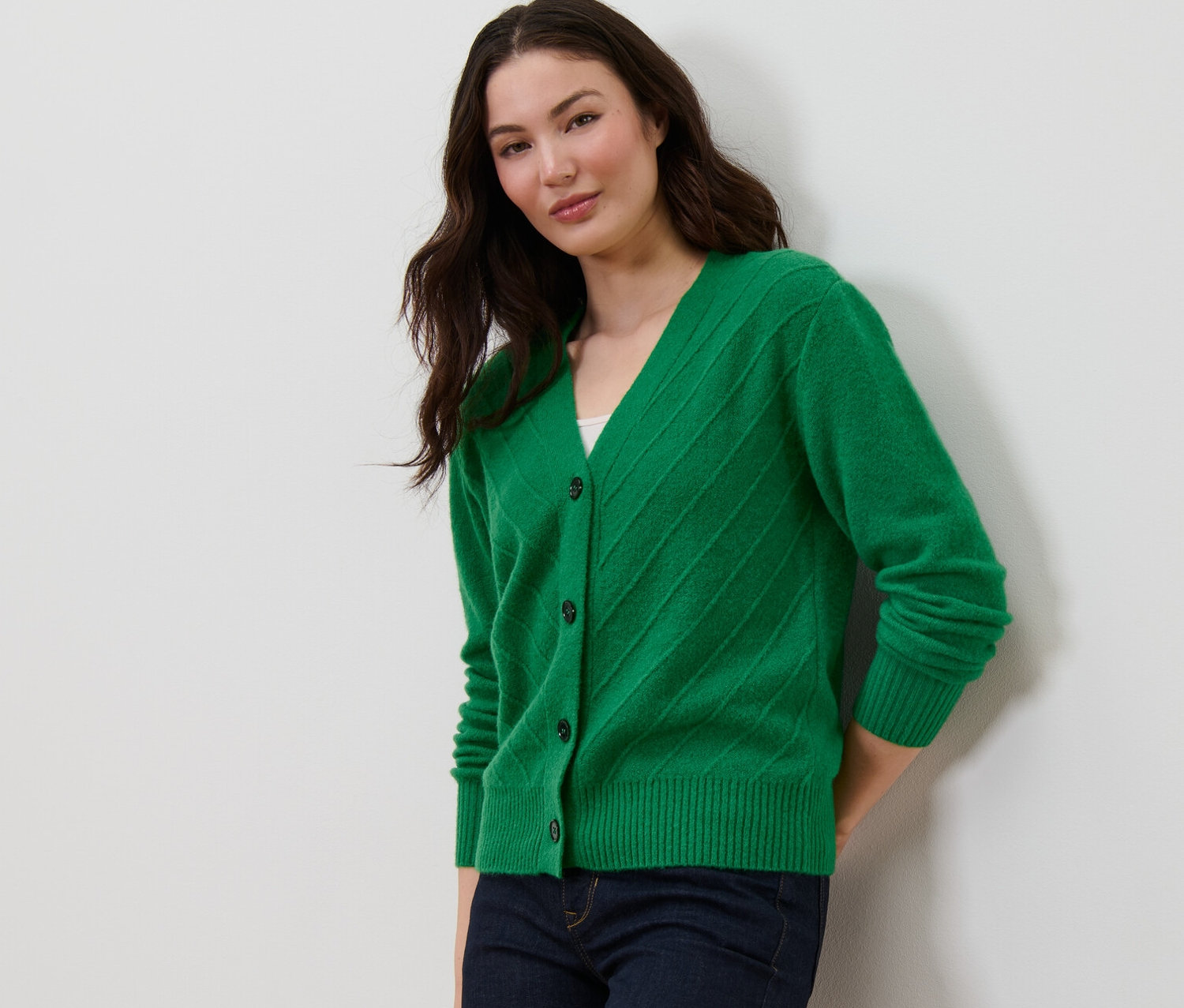 Nő pózol kötött mintás, zöld kardigánban és sötétkék farmerban.