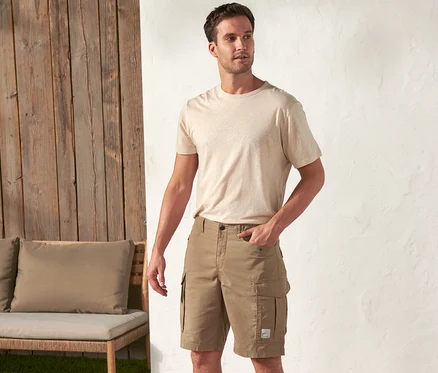 Egy férfi áll a szabadban, bézs pólót és khaki színű Férfi kültéri rövidnadrág, Workwear rövidnadrágot visel.