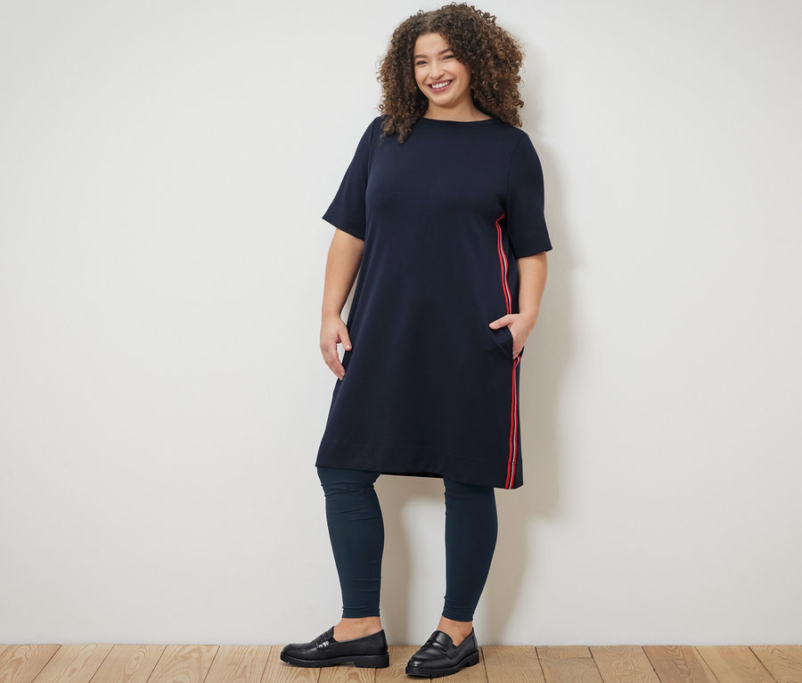 Nő áll a sötétkék, csíkos női lezser ruhában és leggingsben.