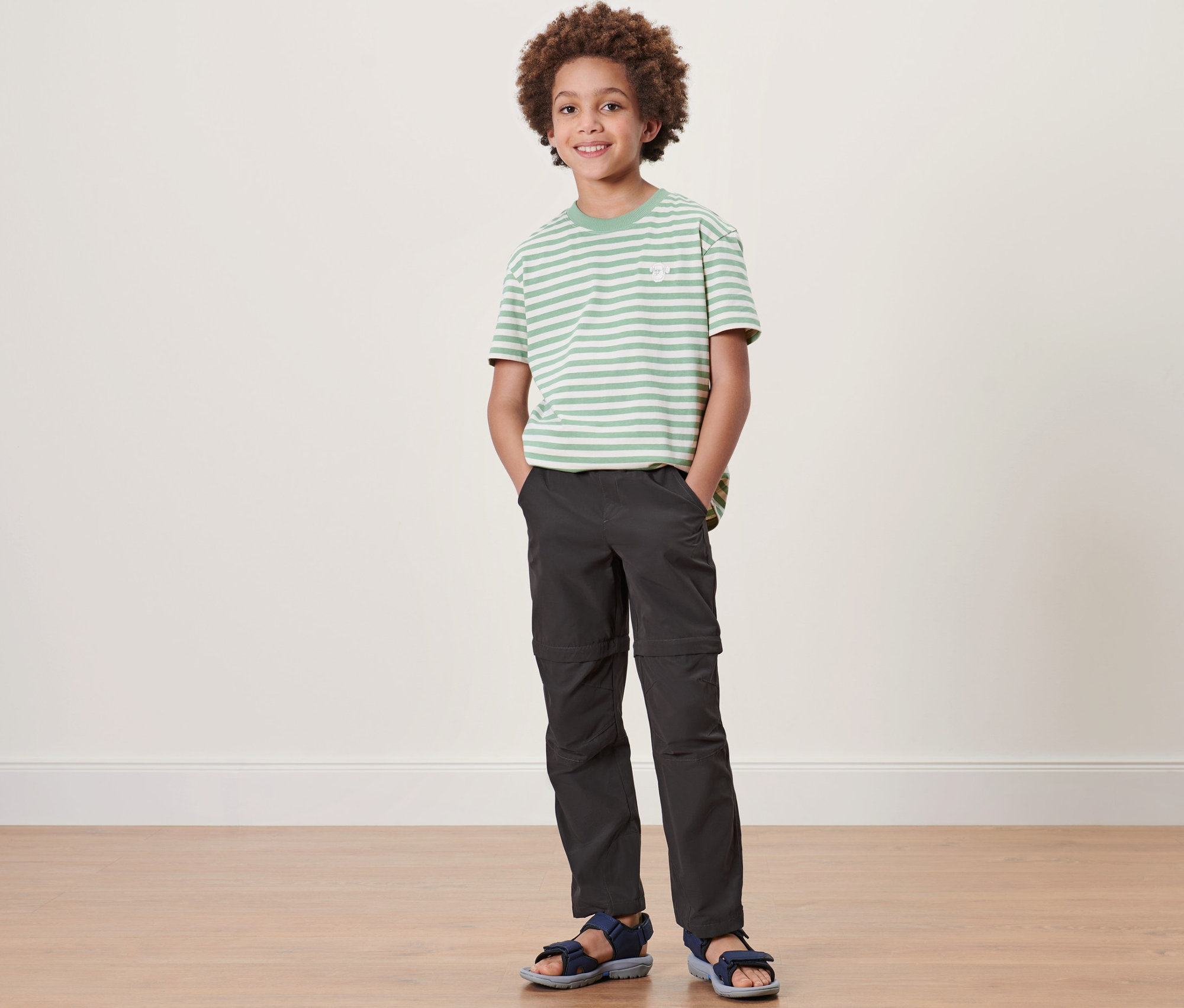 Egy fiú áll, gyermek túranadrágot, csíkos pólót és szandált visel.