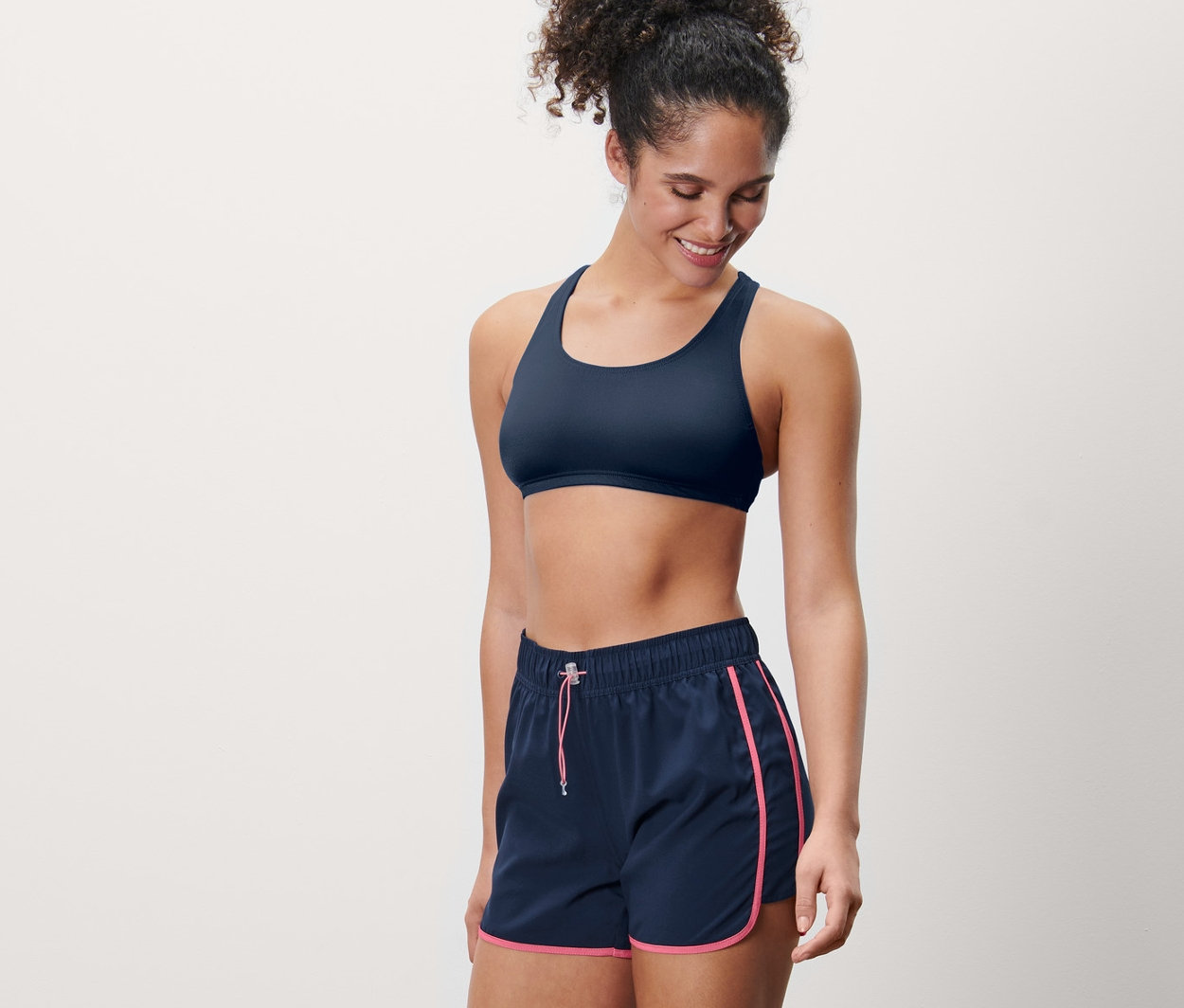 Mosolygó nő fürdőnadrágot és sportmelltartót visel.