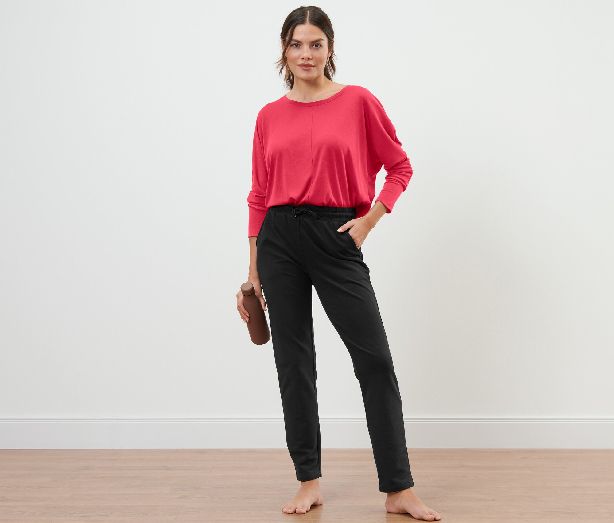 Nő áll, kezében vizes palack, fekete szabadidőnadrágot visel.