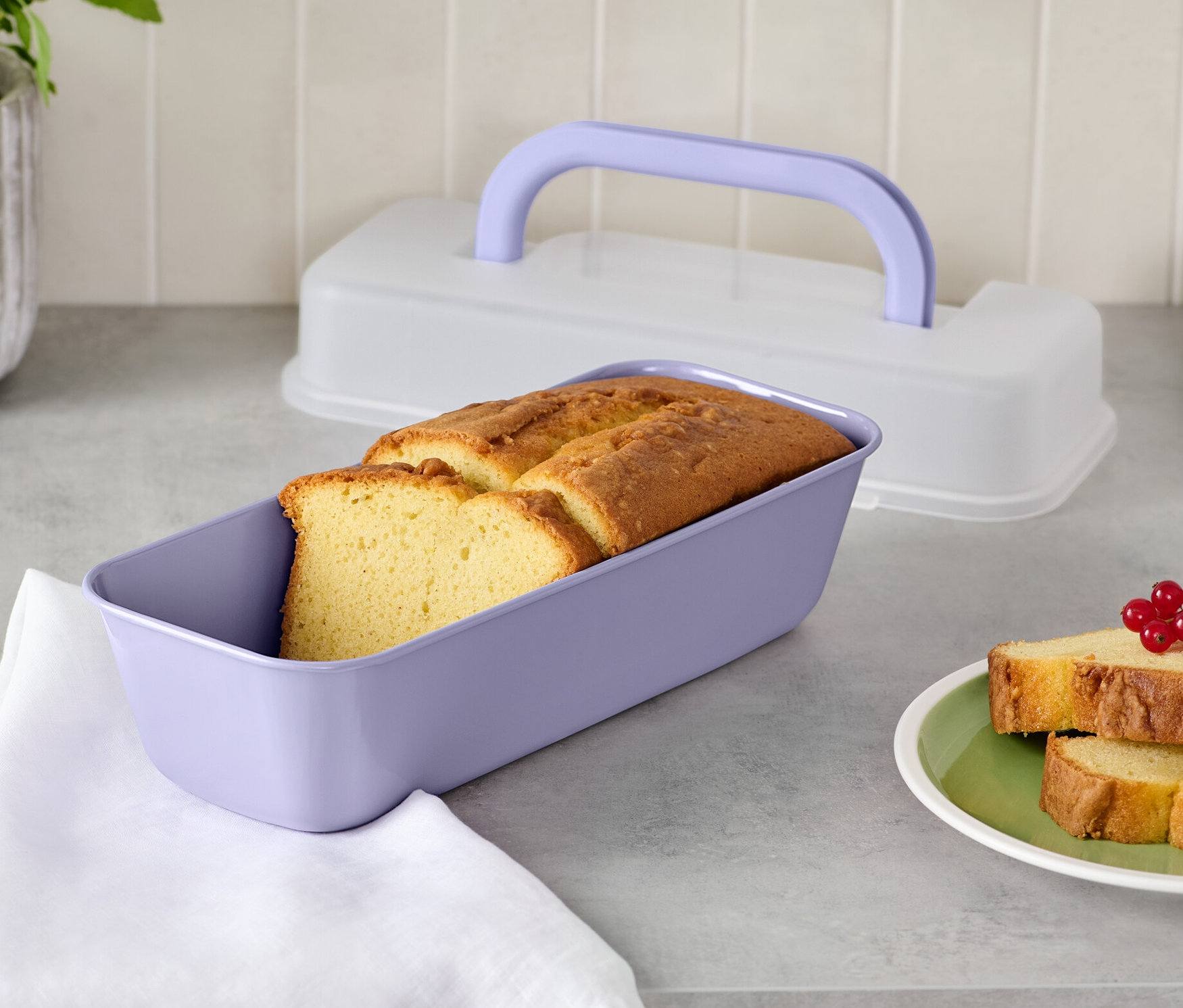 Kenyér egy lila fedeles sütőformában és két szelet kenyér egy tányéron.