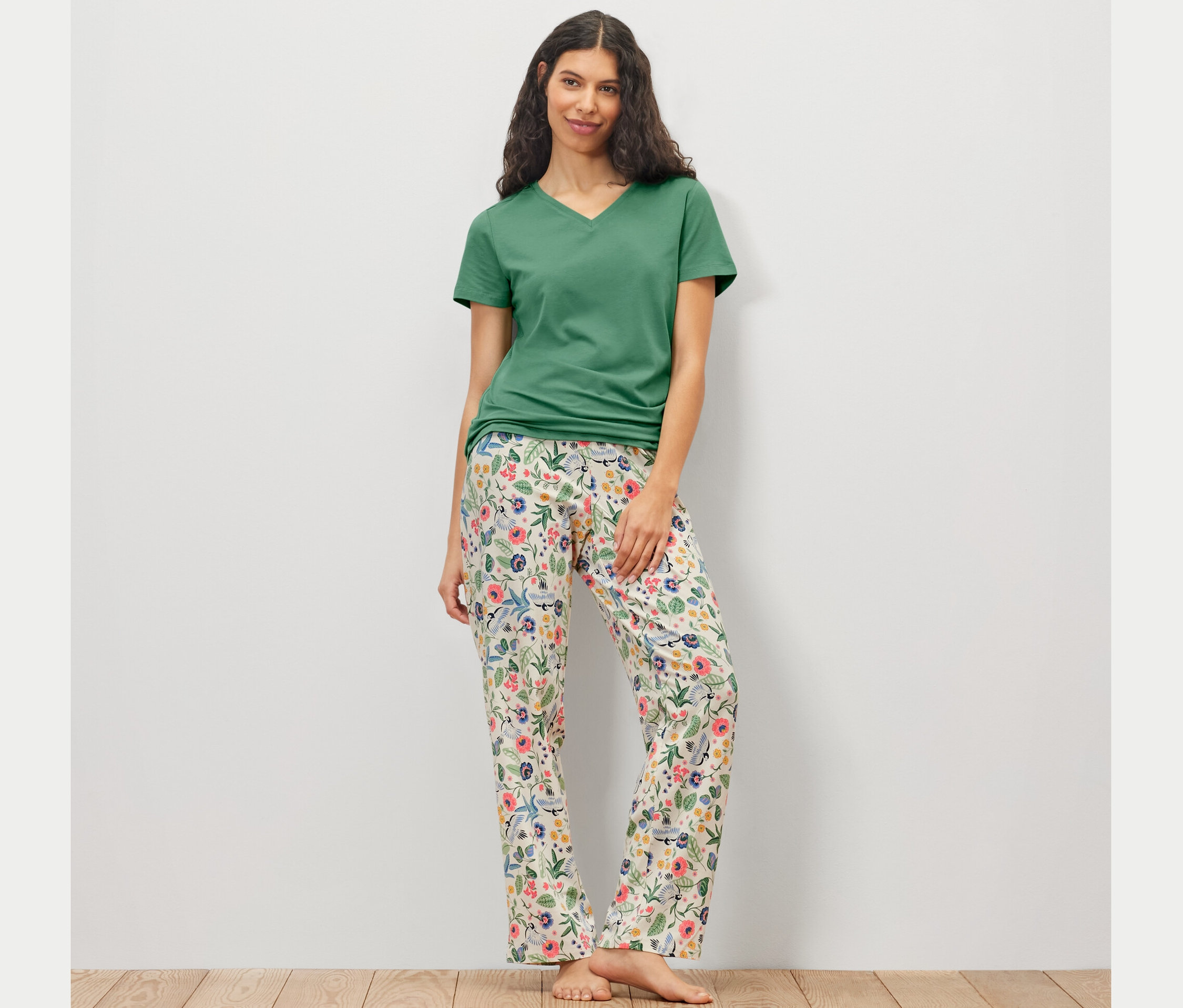 Nő virágos nadrággal és zöld pólóval visel női pizsamát.