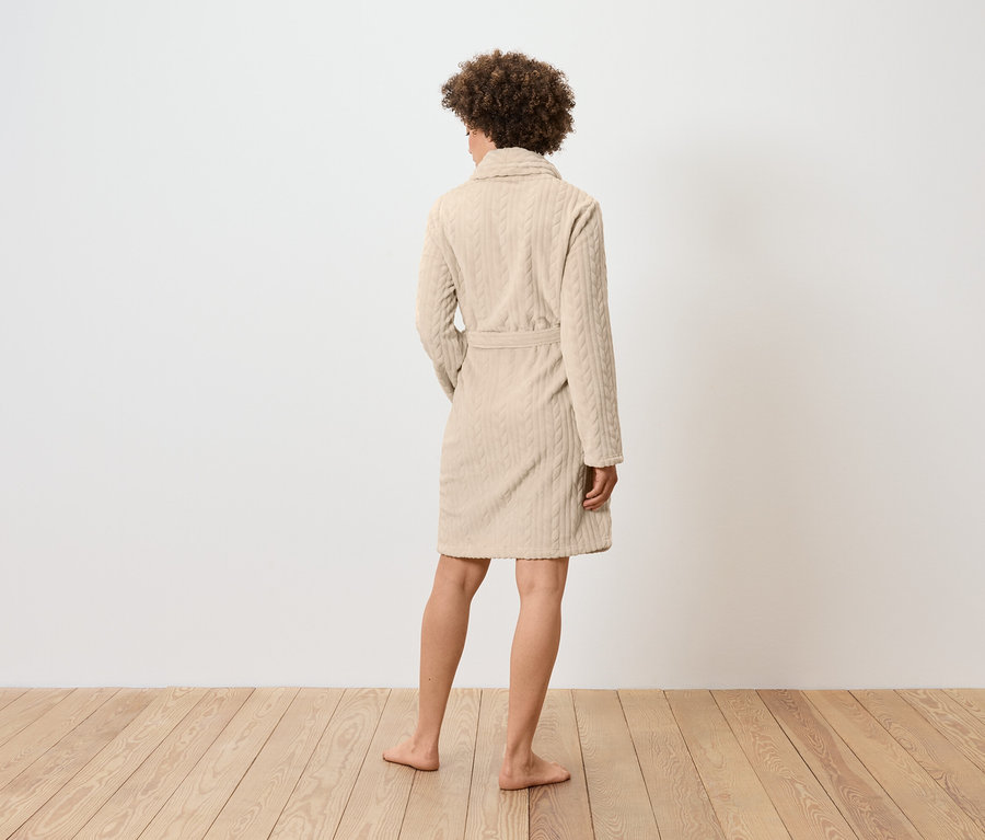 Hátulnézetből egy nő bézs színű, fonott mintás köntösben.