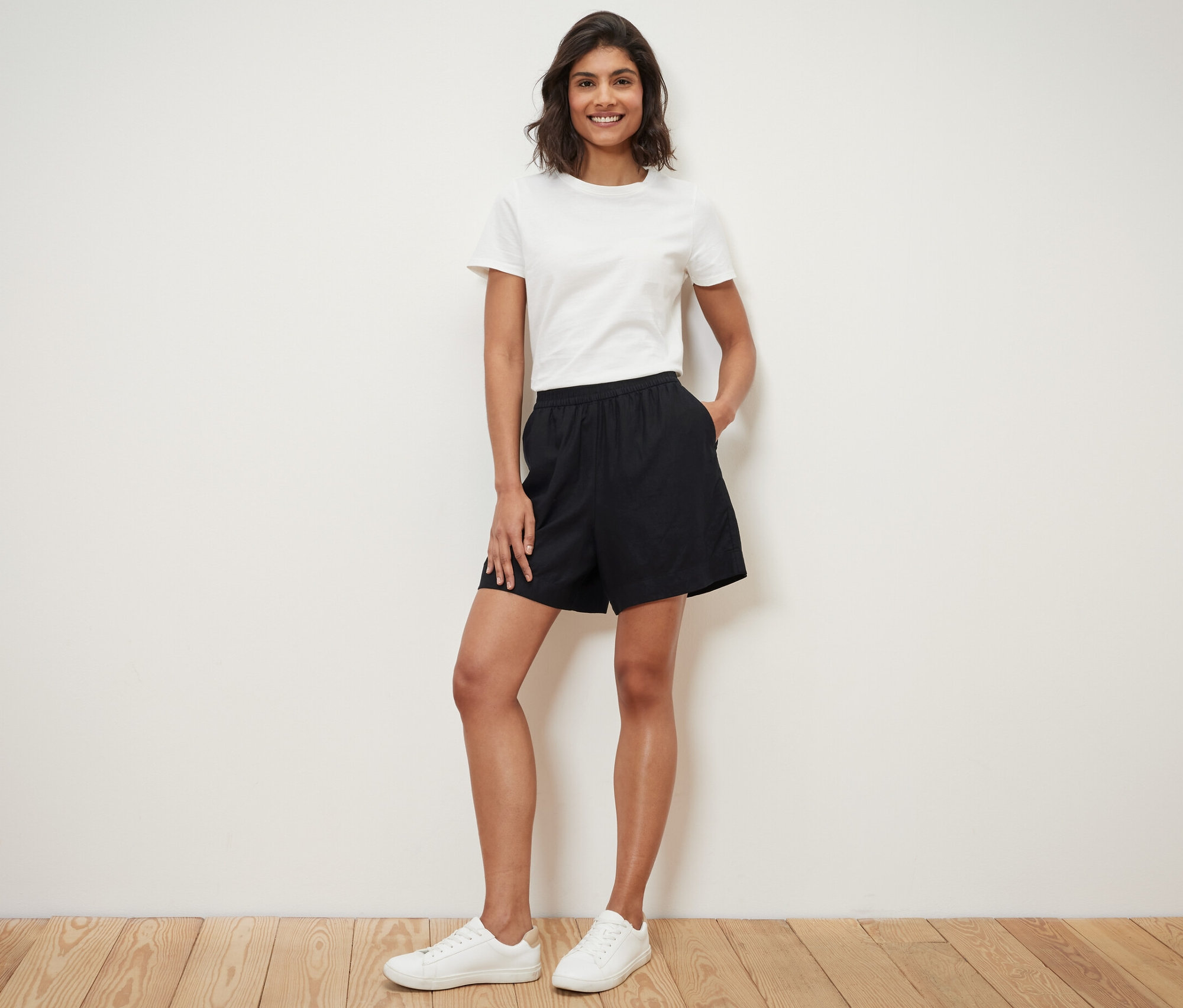 Nő áll, kezével a fekete lenvászon rövidnadrág zsebében.