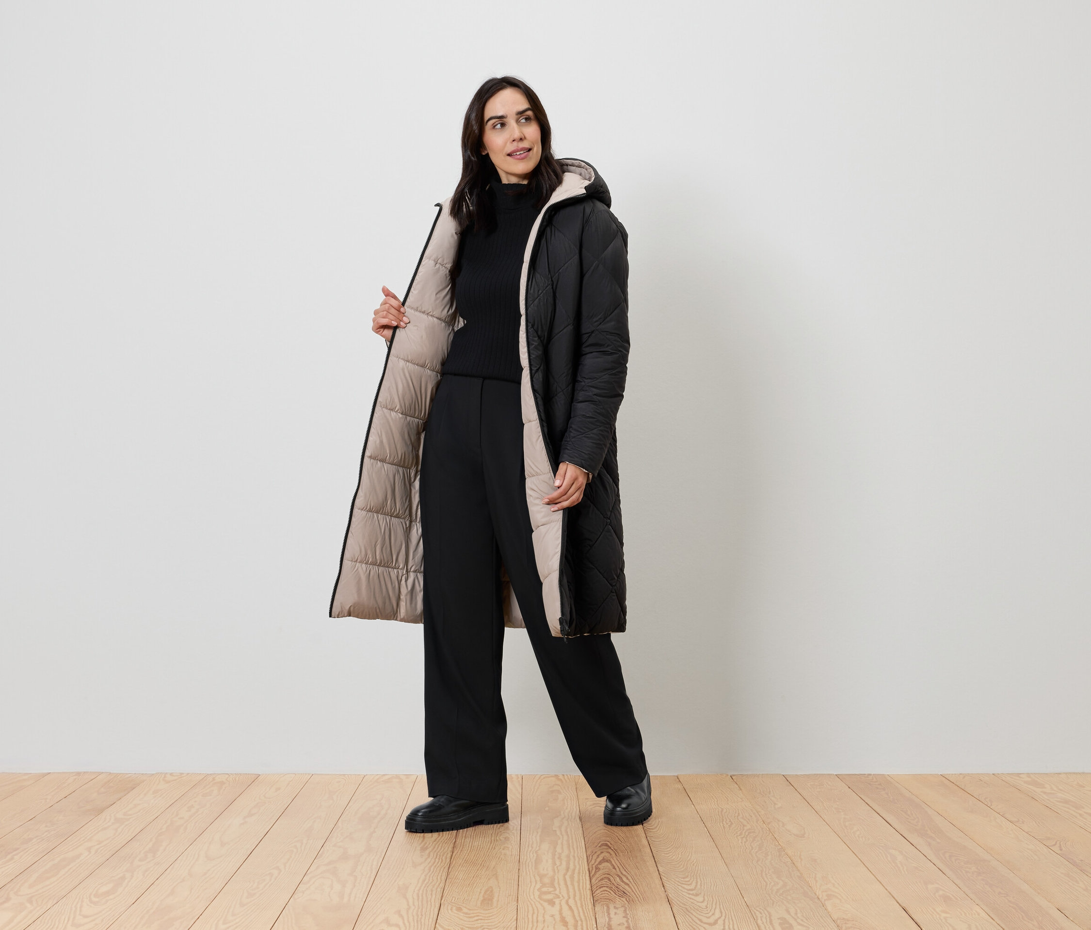 Nő pózol fekete kabátban bézs béléssel, fekete garbóban és fekete nadrágban.