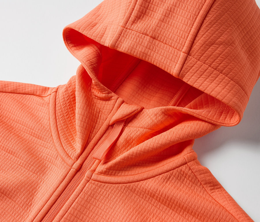 Egy narancssárga, kapucnis funkcionális felső részletfotója.