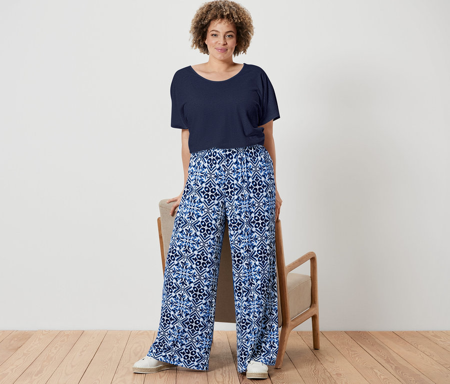 Nő pózol tengerészkék len-keverék pólóban és kék, mintás, női bőszárú nadrágban.