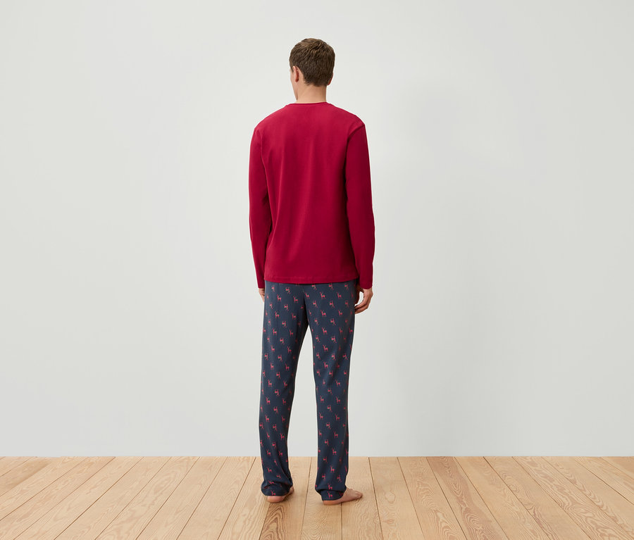 Egy férfi hátulról látható, piros, hosszú ujjú pizsama felsőt és sötétkék, rénszarvas mintás pizsama alsót visel.