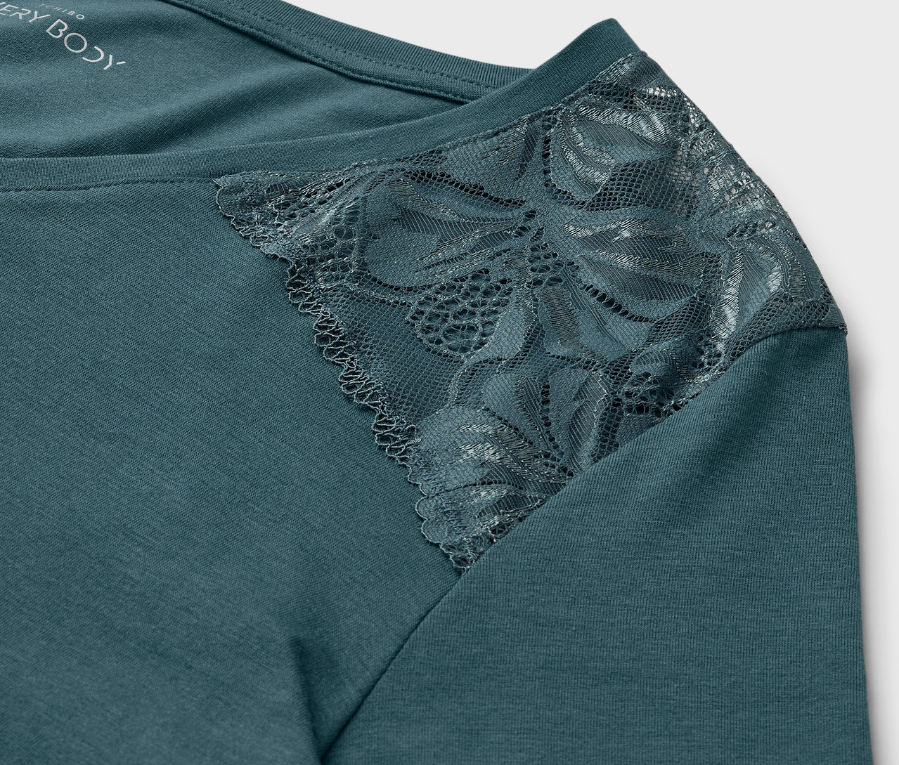 Egy kékeszöld felső részlete csipkével a vállán.