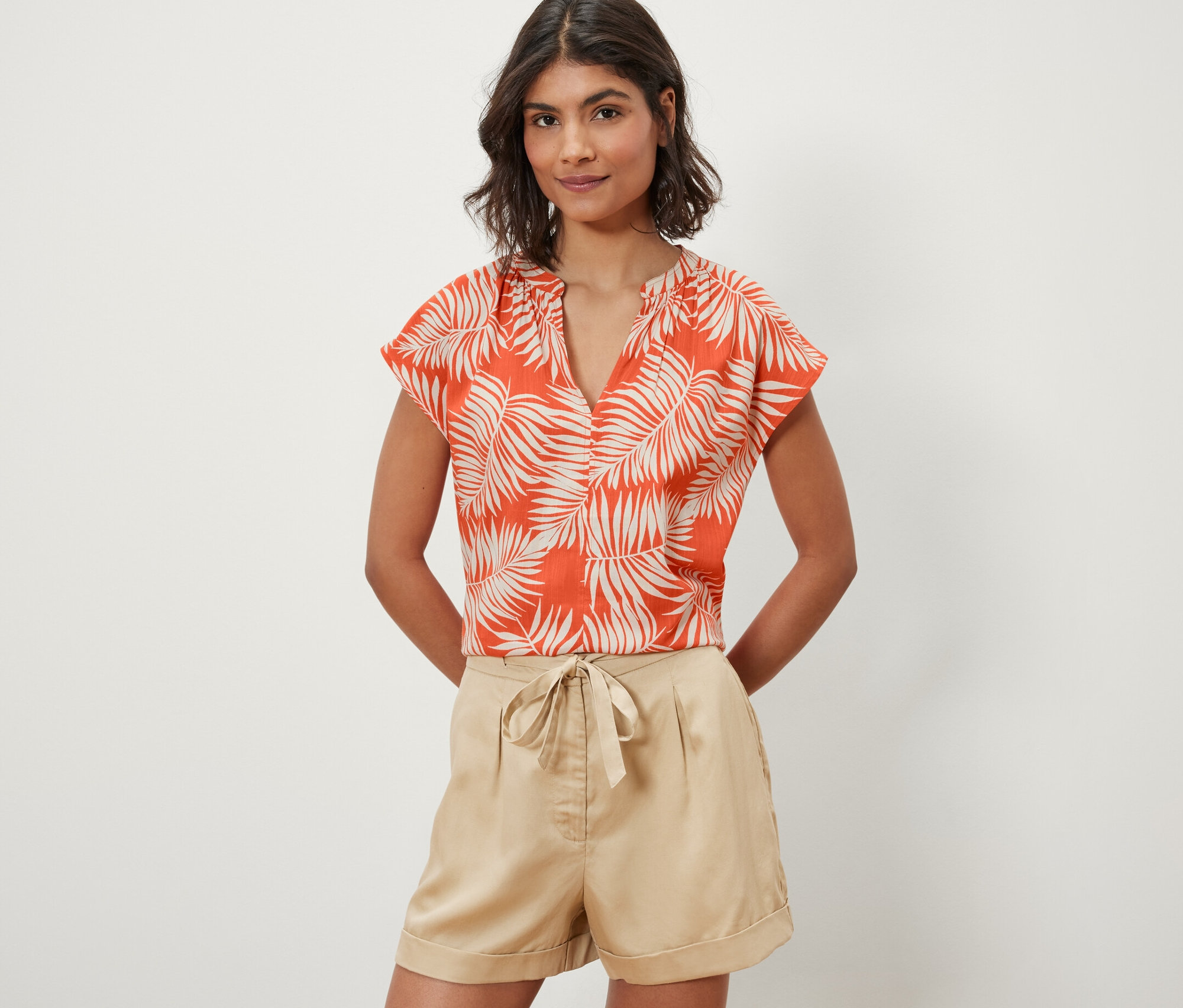 Nő visel egy narancssárga, nyomott mintás, rövid ujjú blúzt.