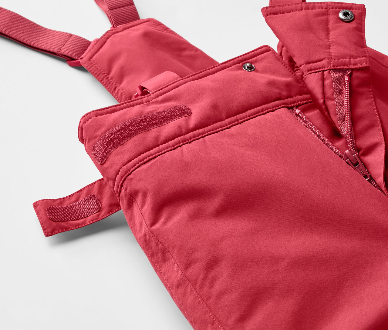 Egy piros, kantáros síelőnadrág részlete cipzárral.