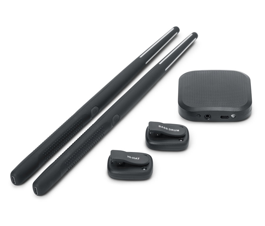 Két fekete dobverő fekszik egymás mellett. Egy fekete hangfal és két kis fekete dobpad, az egyik BASS DRUM felirattal, a másik HI-HAT felirattal szintén látható.