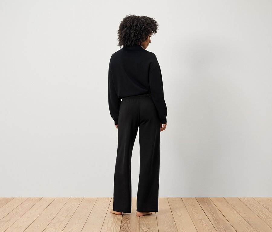 Egy afro frizurás nő hátulról látható fekete pulóverben és fekete nadrágban.