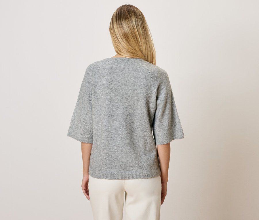 Hátulról látható szőke nő szürke, háromnegyedes ujjú pulóverben és fehér nadrágban.