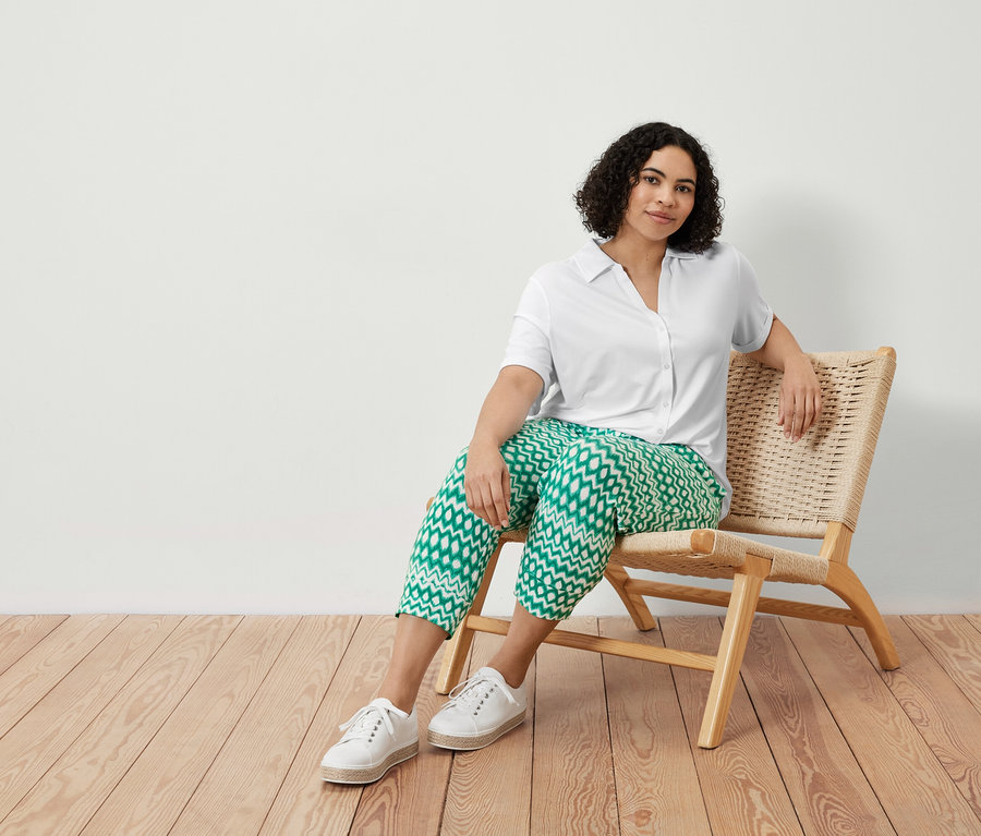 Egy nő egy székben ül, és egy nyomott mintás, 3/4-es jersey nadrágot és egy fehér női pólóblúzt visel.