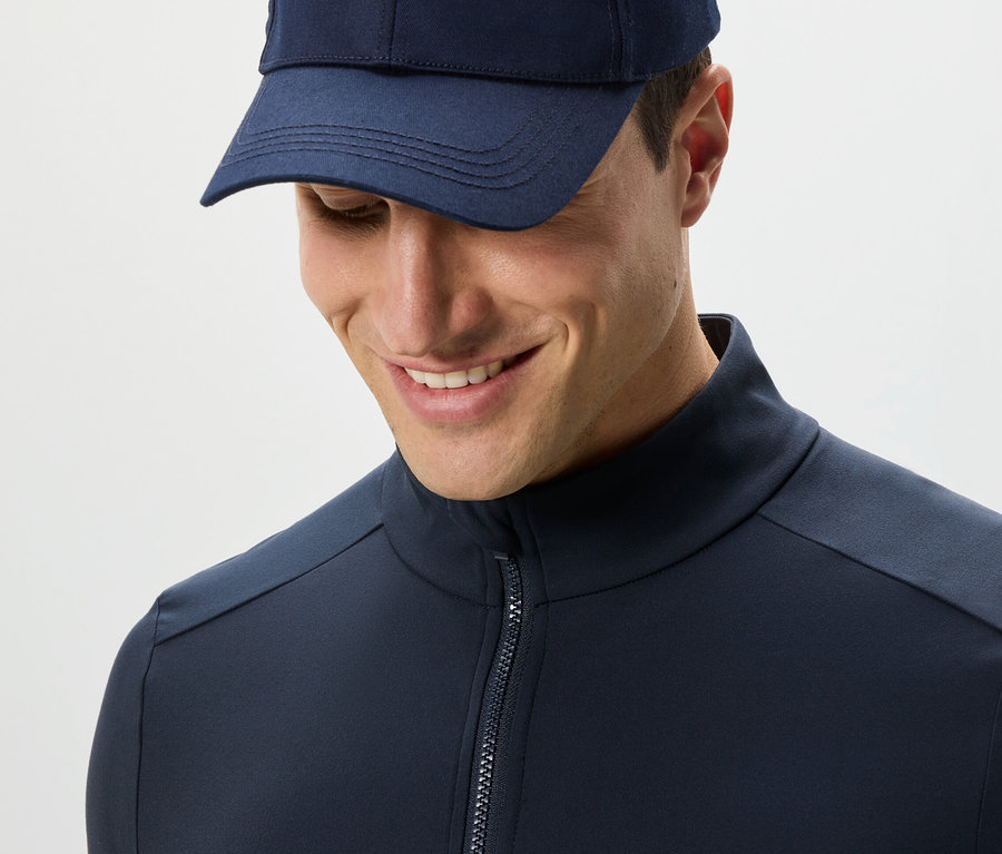 Férfi sötétkék funkcionális felsőben és sapkában lefelé néz.
